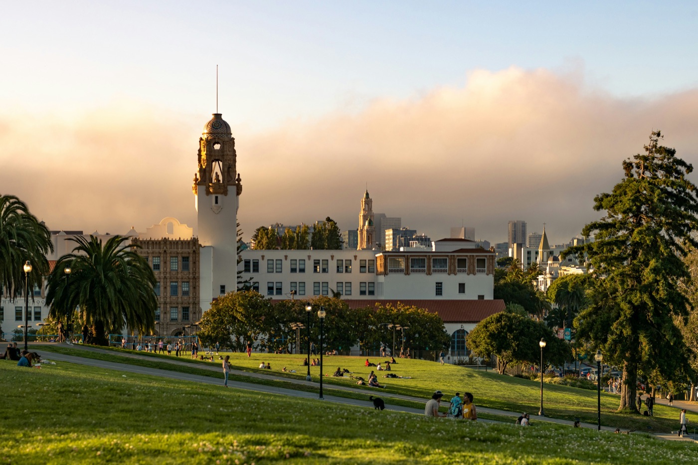 Dolores Park at golden hour, people gathered across the grass under a wide sky.