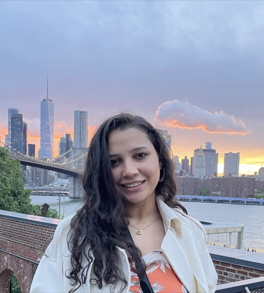 Kanica, the founder of Roohbrew, smiling outdoors at sunset with a city skyline behind her.